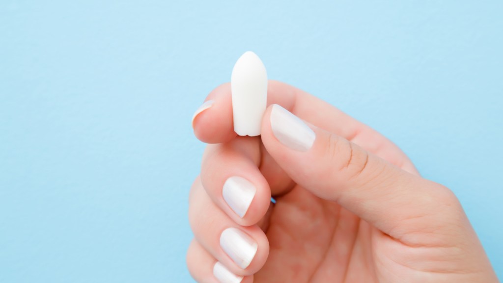 A close up of a woman with white nail polish holding a boric acid suppository, one of the best home remedies for bacterial vaginosis