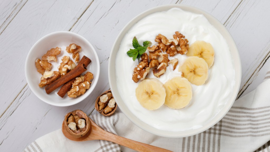 A bowl of yogurt, one of the best home remedies for bacterial vaginosis, topped with sliced bananas and walnuts on a wood table
