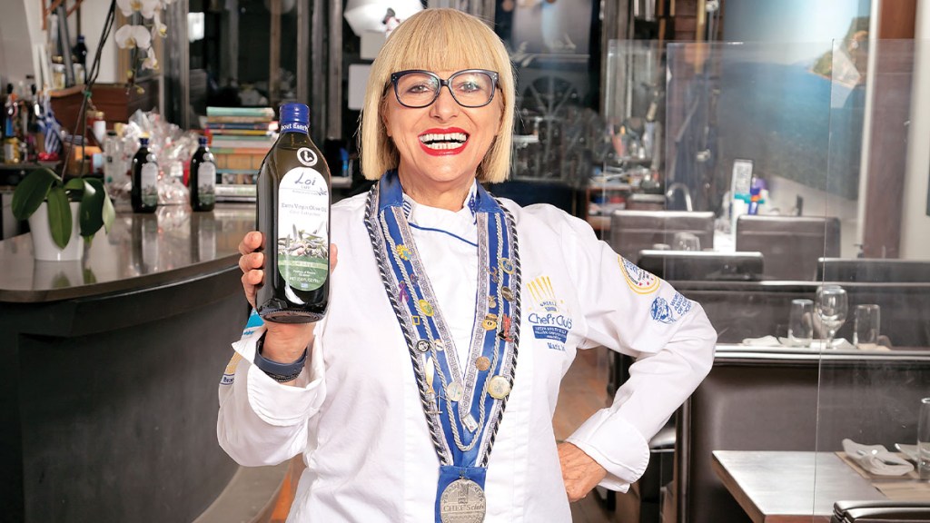Chef Maria Loi, who used olive oil for weight loss, standing in a kitchen with a bottle of olive oil