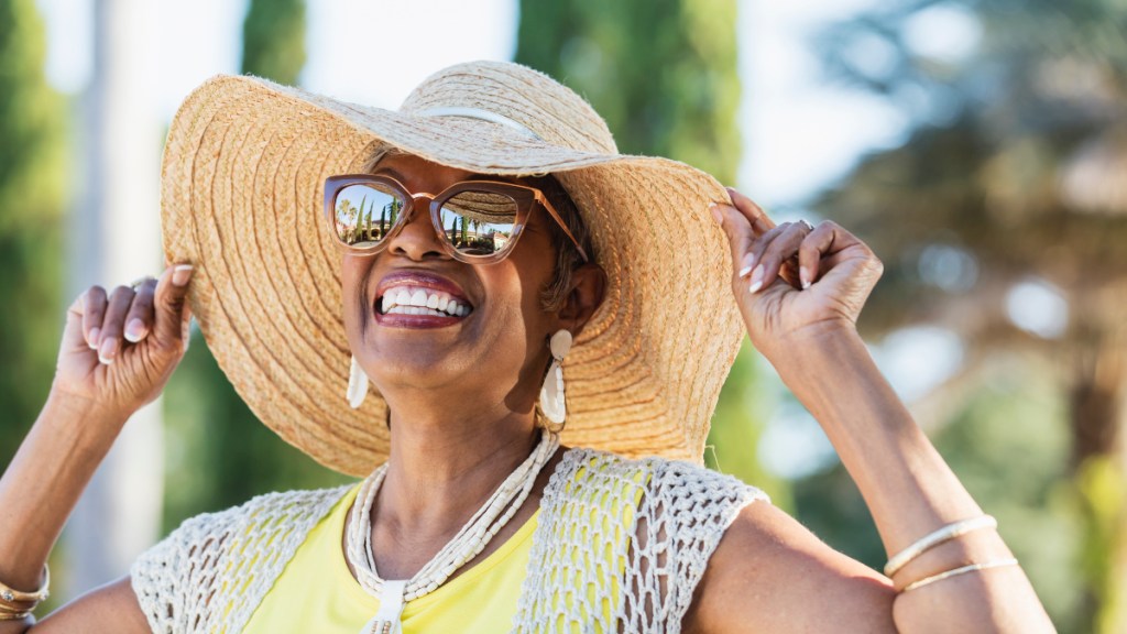 A smiling woman in a wide brim hat and sunglasses who is preventing cataracts naturally
