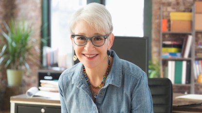 A grey-haired woman wearing glasses and a chambray top who takes steps to prevent cataracts naturally