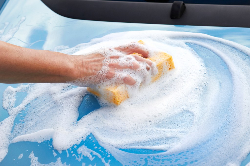 Woman's hands cleaning car with sponge