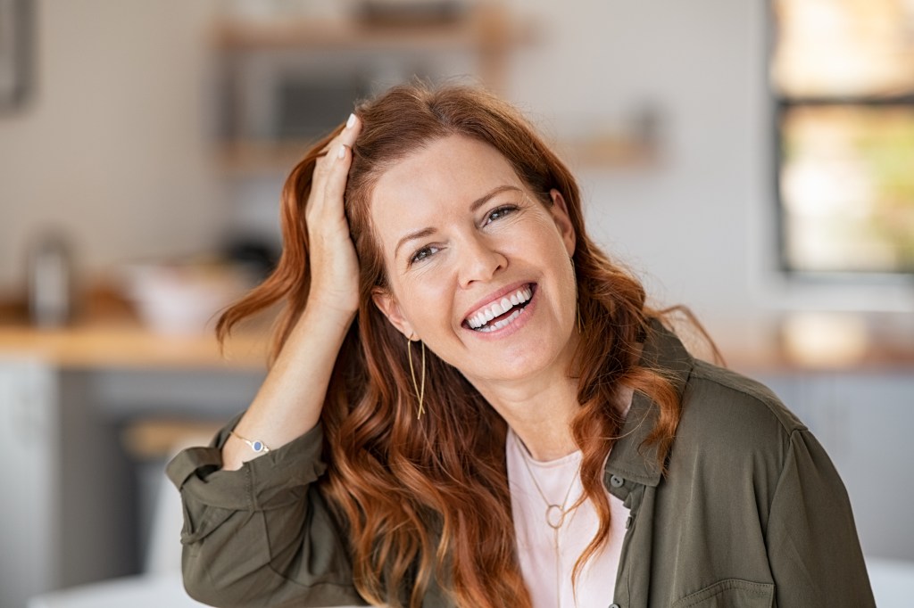 Photo of a redheaded woman smiling and touching her scalp after using an anti-dandruff apple cider vinegar hair treatment