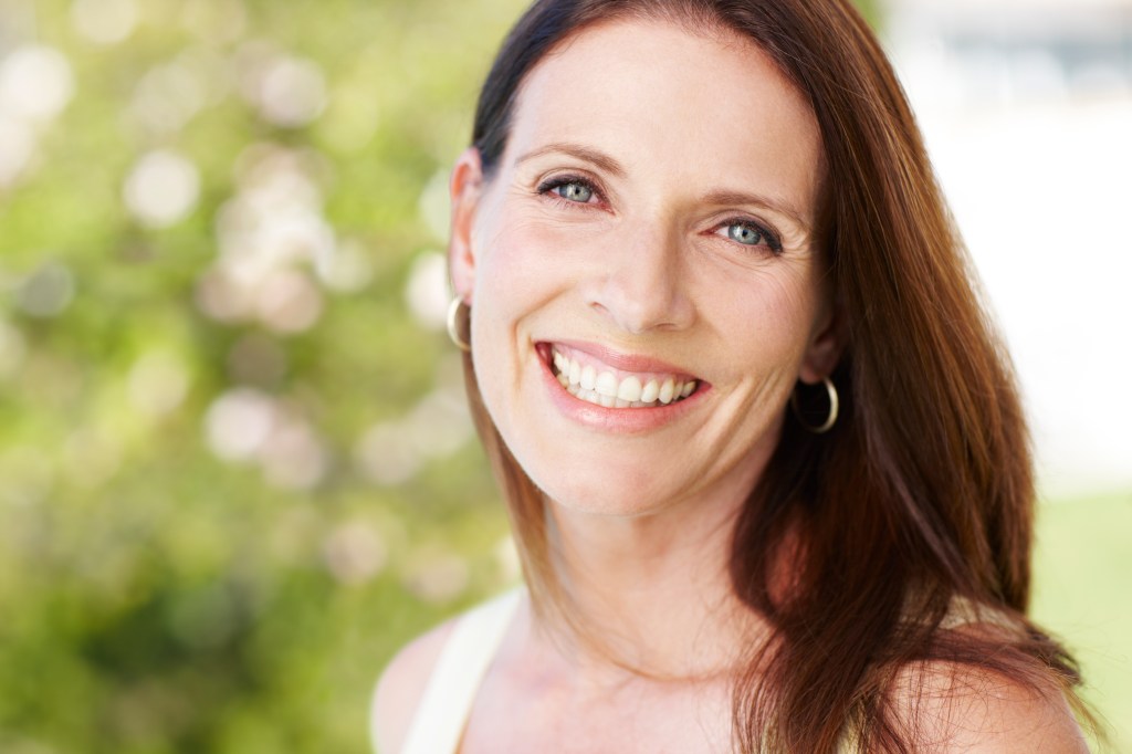 Brunette woman who is outside and is smiling. Her skin looks free of redness after using apple cider vinegar skin care