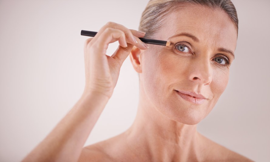 Mature woman holding eyeliner pencil up to eye