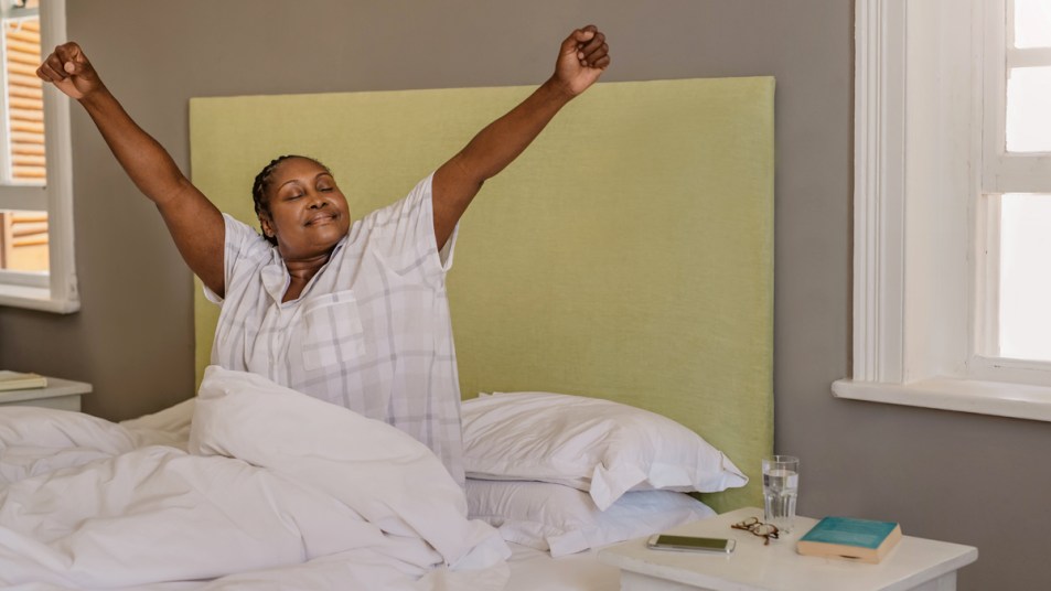 Woman sitting up and stretching arms out in bed