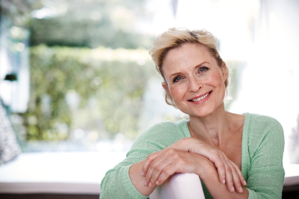 Mature woman with blond hair smiling with her arms crossed over a chair