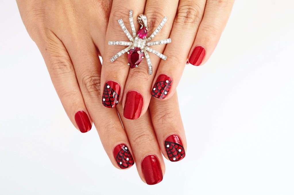 Red nails with black spiderweb design and rhinestones.