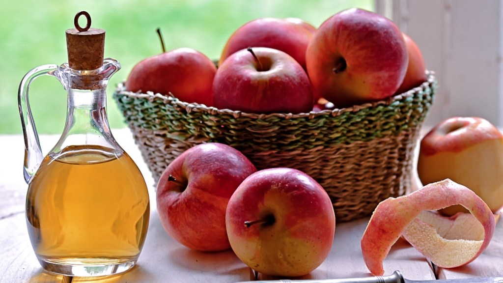 A clear bottle of apple cider vinegar next to a basket of red apples
