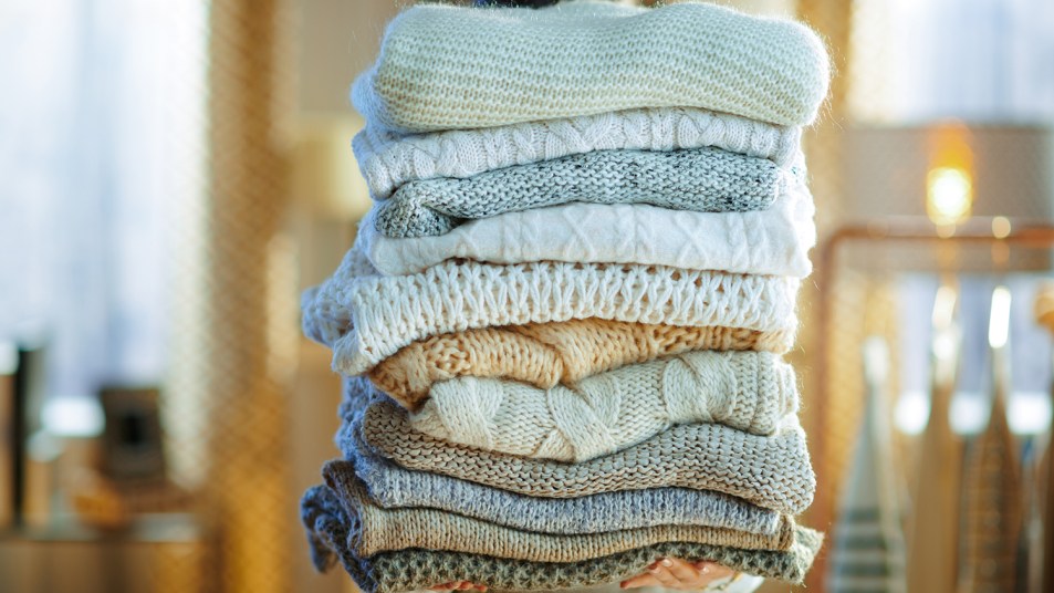woman holding a pile of fall wardrobe sweaters