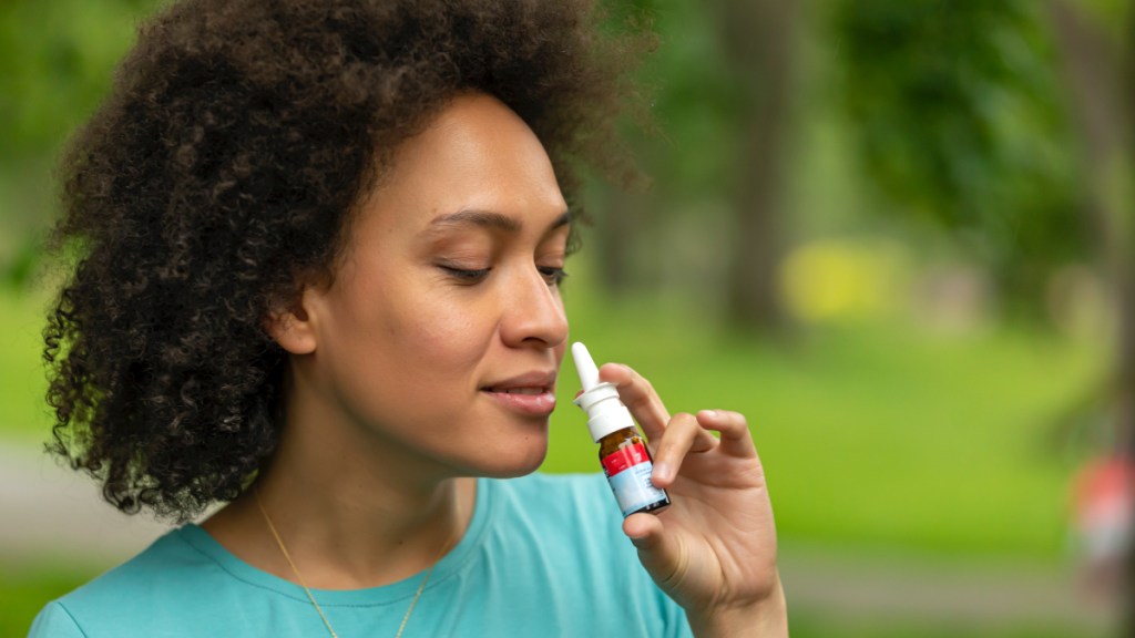 A woman closing her eyes while holding a nasal spray bottle, which helps stop a runny nose in 5 minutes