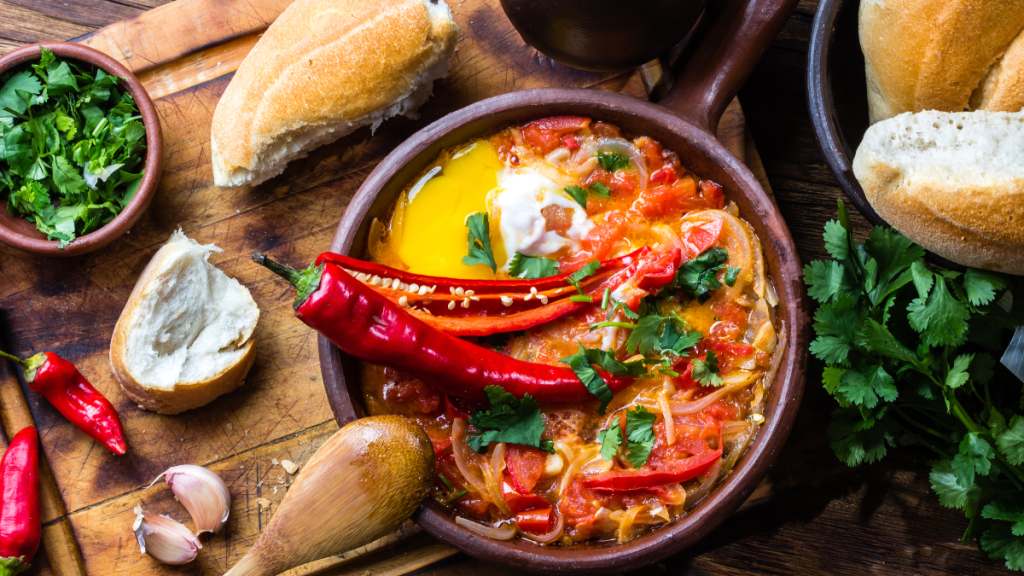 A bowl of spicy chili peppers (which can cause a runny nose) and veggies on a wooden table with bread