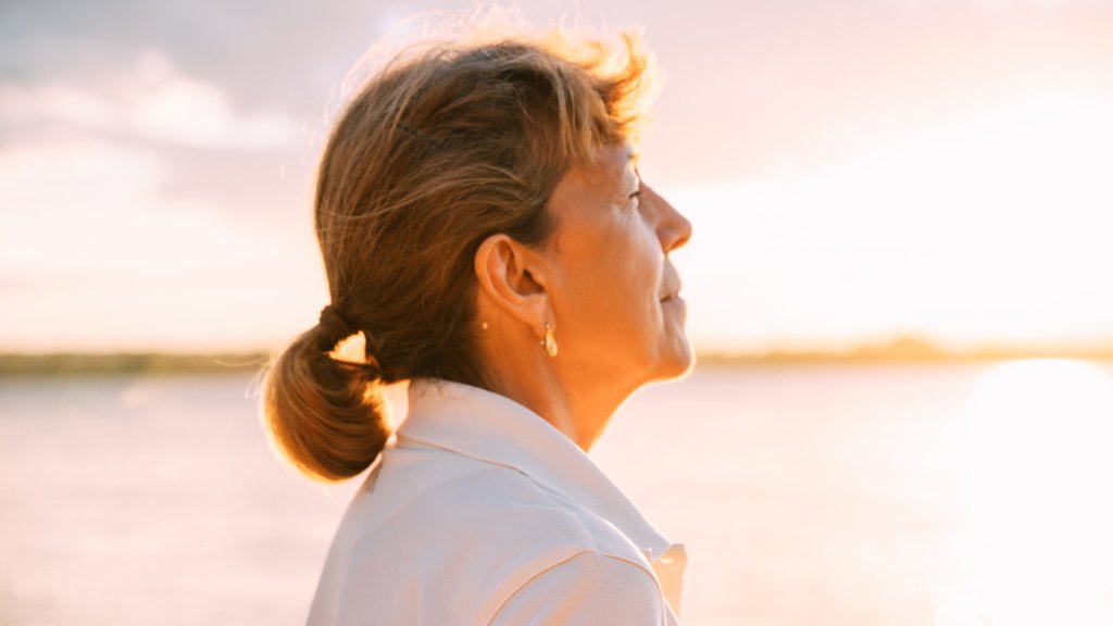 middle-aged woman closes her eyes near at sunrise, feeling the strength and comfort of a higher power