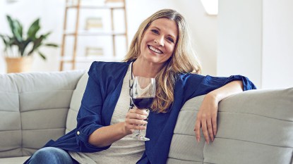 Smiling woman sitting on couch and holding a glass of resveratrol-rich red wine