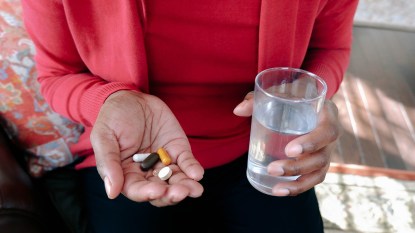 Close-up of woman preparing to take her daily dose of pills/supplements with glass of water