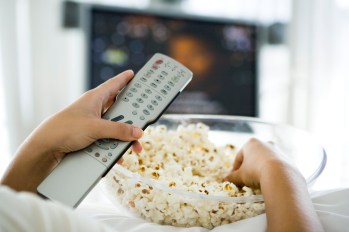 Person watching television, holding remote control and bowl of popcorn