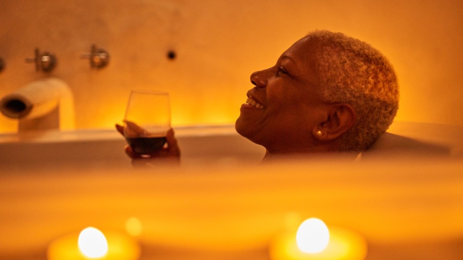 mature woman with short gray hair in bath holding glass of wine, enjoying a beauty treatment