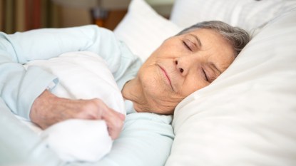 mature woman with short hair sleeping in bed under white sheets