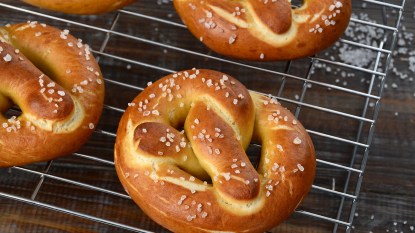 Traditional German pretzels, sprinkled with coarse salt, sit on a cooling rack.