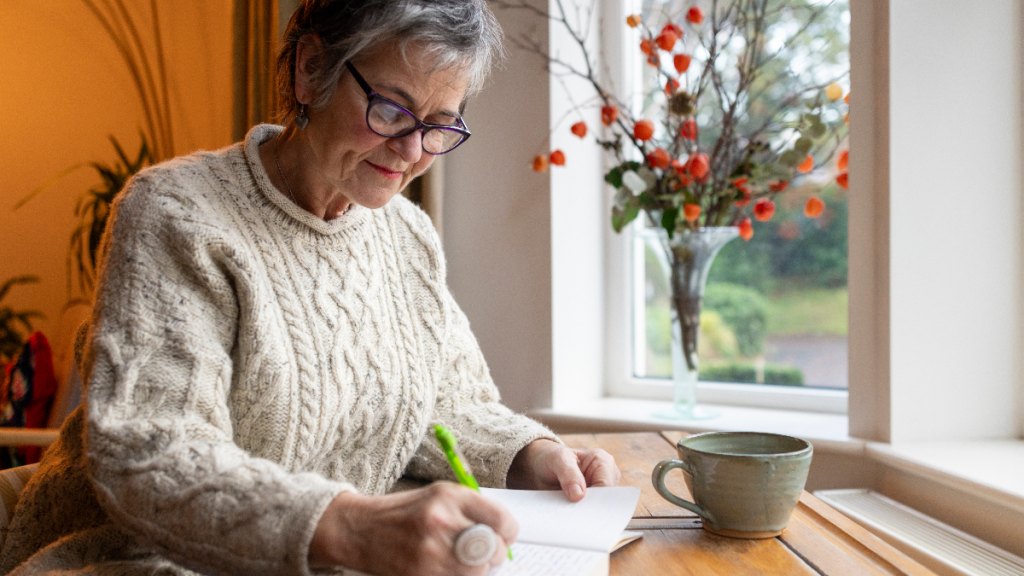 middle-aged woman jots down what brings her joy, as she focuses on beating the winter blues