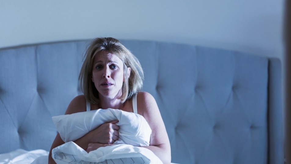 mature woman in bed waking up scared, clutching a white pillow