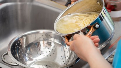 woman separating water from spaghetti with empty silver colander. draining pasta