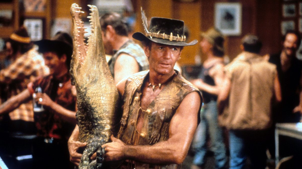 Paul Hogan, 'Crocodile Dundee' filminden bir sahnede barda ölü timsah taşır, 1986.