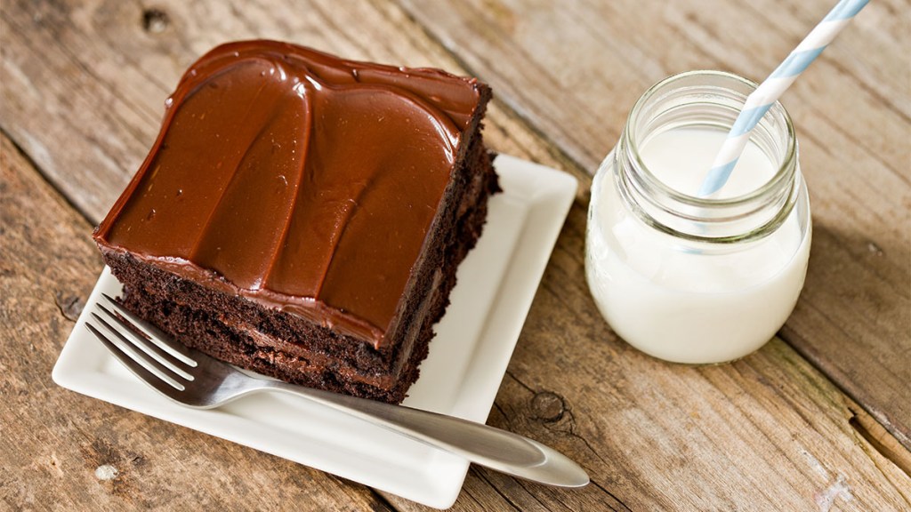 Square piece of chocolate mayonnaise cake on a plate next to a glass of milk