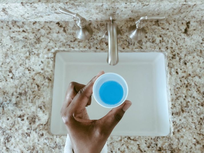 close up of hand holding cup of mouthwash over a sink