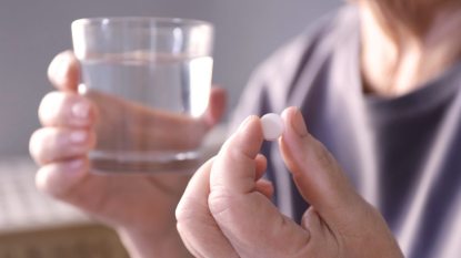 close up of mature woman holding a pill in one hand and glass of water in the other, senolytic drugs concept