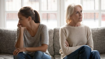 older mother and adult daughter sitting on sofa facing away from each other