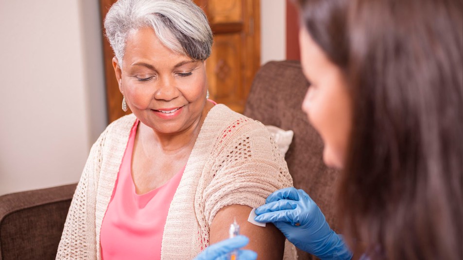 Home healthcare nurse giving covid vaccine to senior adult woman.