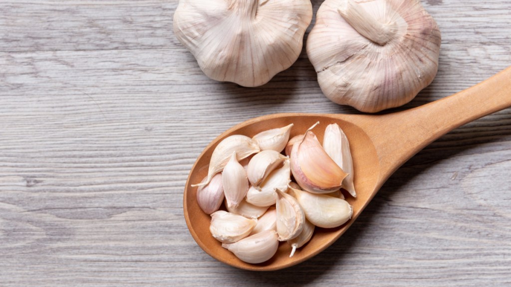 Gloves of garlic in a wooden spoon beside fresh, whole garlic