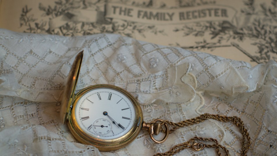 Family Heirloom Gold Pocket Watch and Watch Fob Laying on White Eyelet Handkerchief