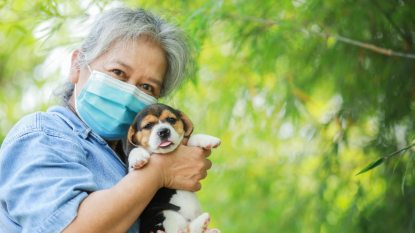 senior woman with mask on holding puppy, dog allergy vaccine concept