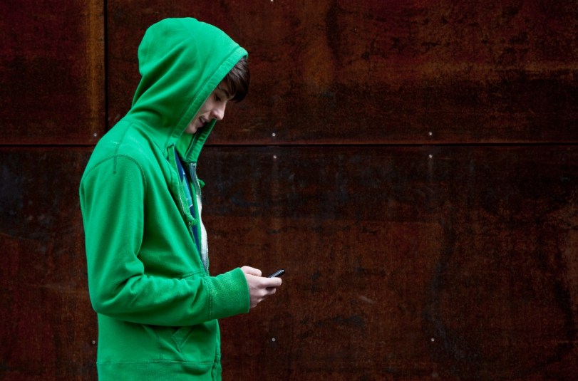 Teen in hooded sweatshirt text messaging