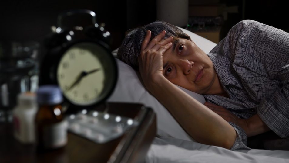 senior woman lying awake in bed, clock on nightstand, concept for sleep apnea