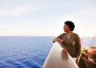 Mature African American woman leaning on rail on deck of cruise ship, peering out into the ocean
