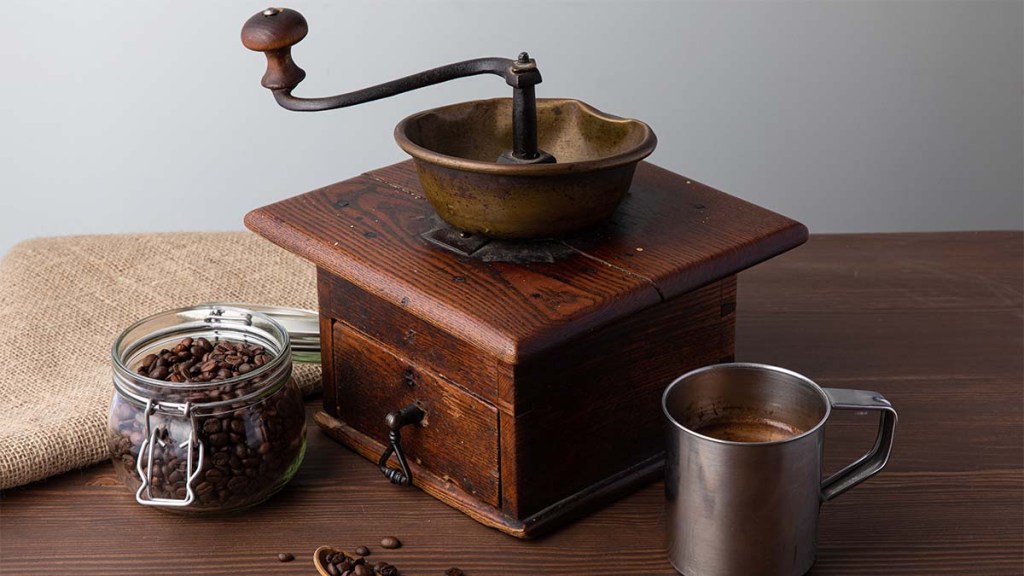 An-antique-coffee-grinder-sitting-on-a-wooden-table-surrounded-by-coffee-and-coffee-beans