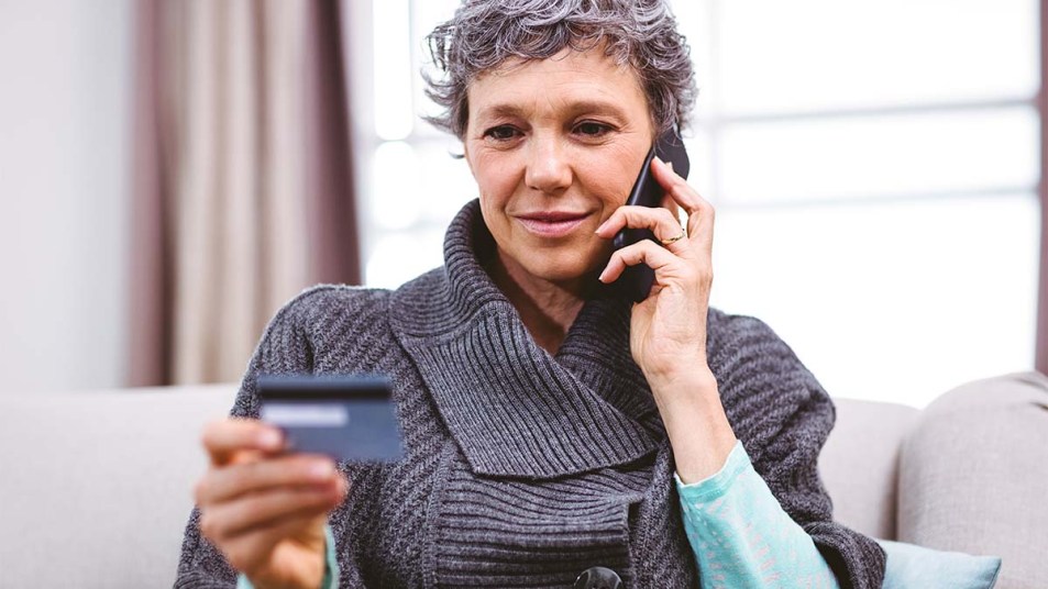 Close-up-of-mature-woman-holding-credit-card-while-talking-on-mobile-phone-at-home-how-to-spot-and-avoid-charity-scams