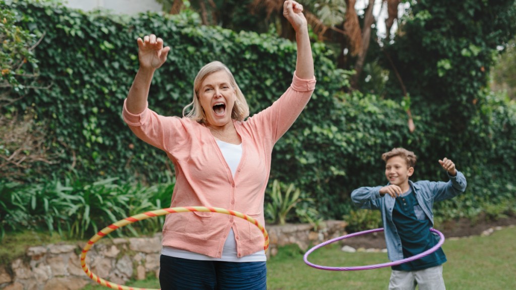 A woman wearing a cardigan with her hands in the air using a hula hoop next to a young boy using a hula hoop