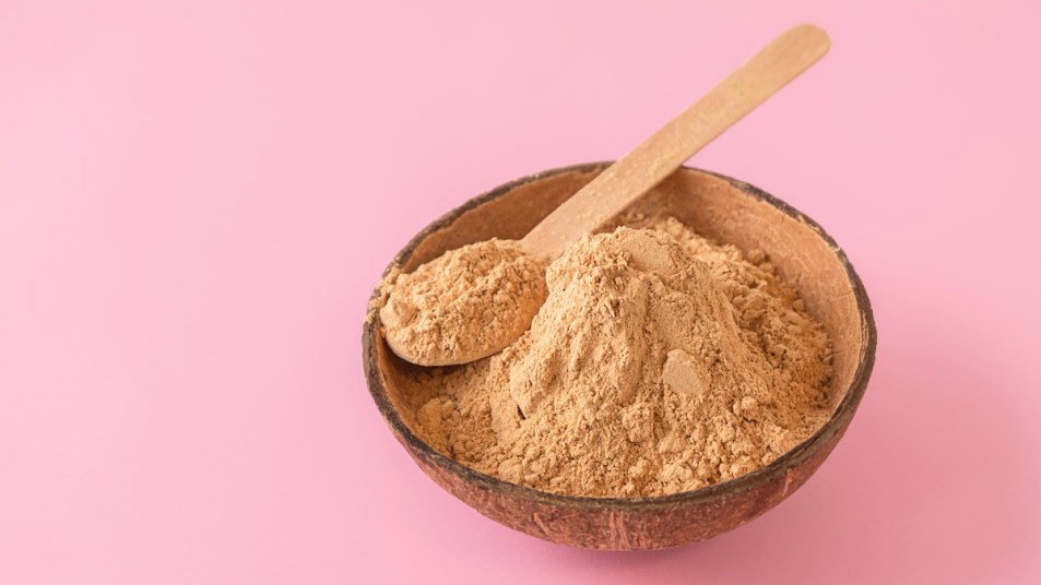 A bowl of maca powder, which benefits females, on a pink background