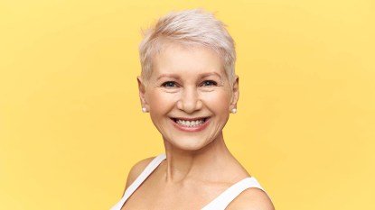 Mature-woman-with-a-pixie-cut-smiling-against-a-yellow-backdrop