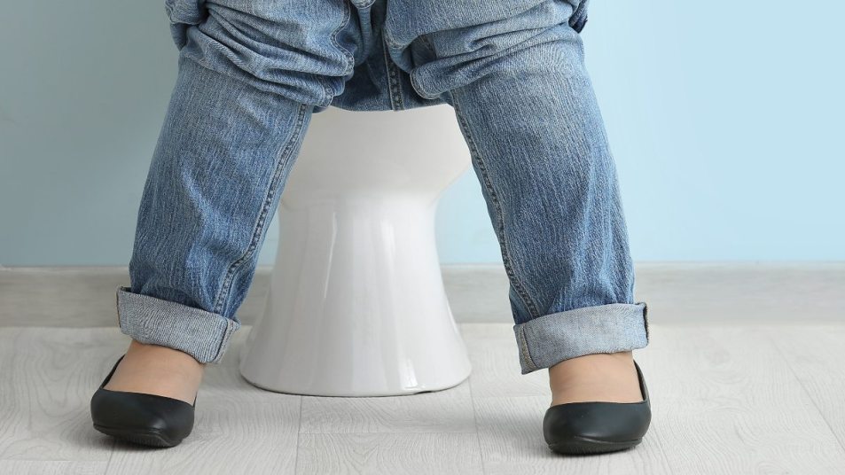 mature woman sitting on a toilet with jeans rolled down, concept for sitting vs squatting to pee