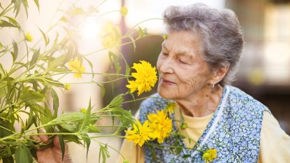 mature woman with short gray hair smiling as she smells yellow flowers - trick for preventing memory lapses