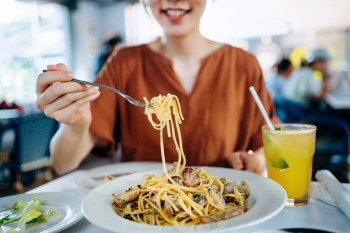 Asian woman eating freshly served linguine pasta with fresh clams for lunch in a restaurant.