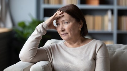 Stressed senior retired woman touching forehead, looking away, feeling doubtful about decision. Unhappy thoughtful middle aged lady sitting on couch, worrying about personal problems alone at home.