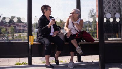 two strangers, mature women at a bus stop drinking coffee and talking