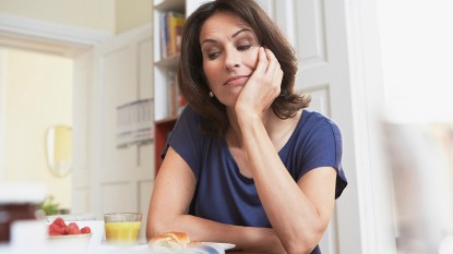 A middle aged woman looking at her breakfast and wondering 'why am I not hungry in the morning?'