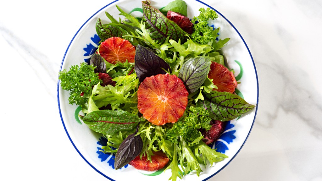 A white bowl filled with leafy greens, which are a potassium-rich food, and sliced fruit